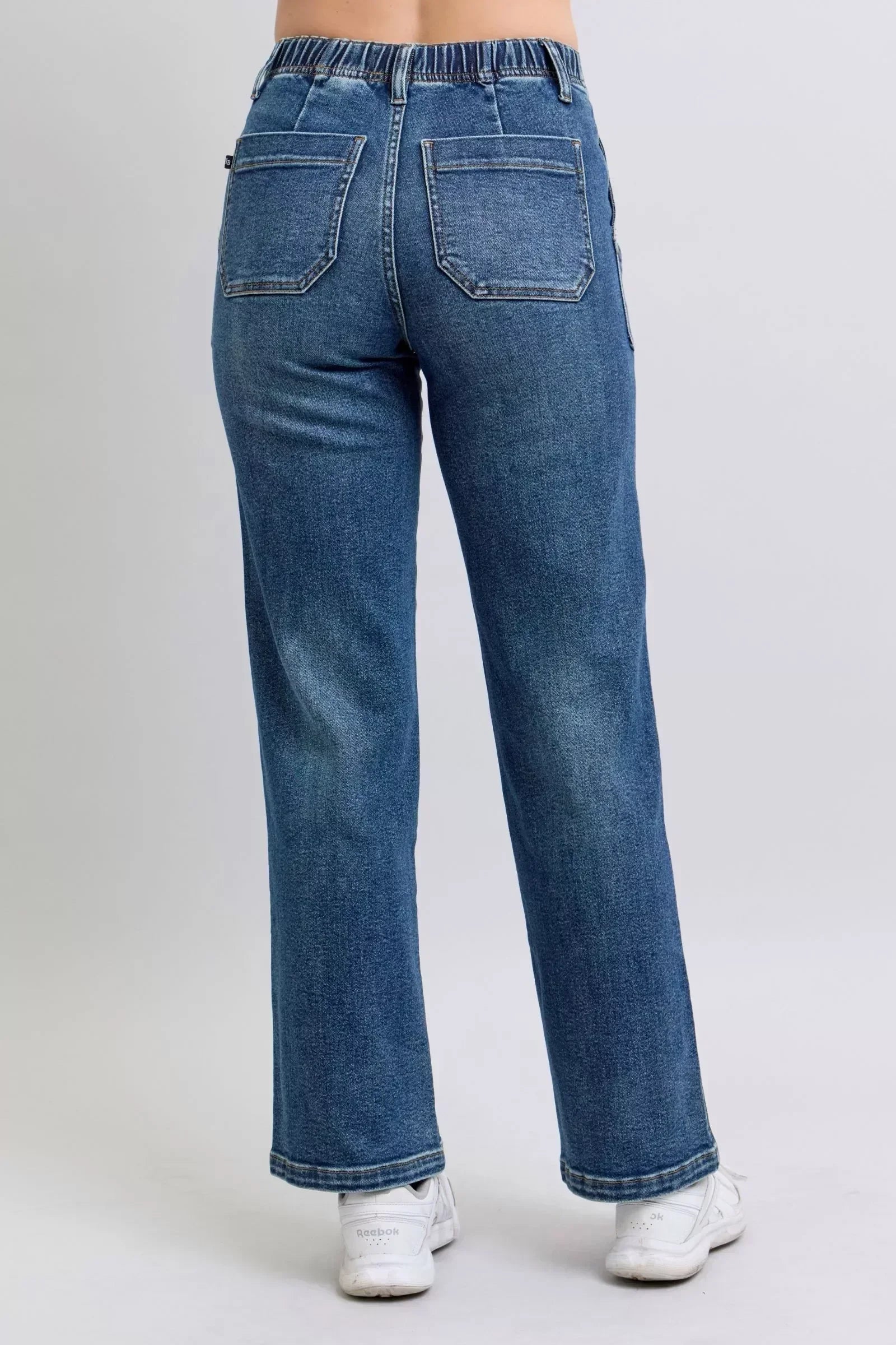 Back view of woman wearing blue straight-leg denim jeans with elastic waistband and white sneakers