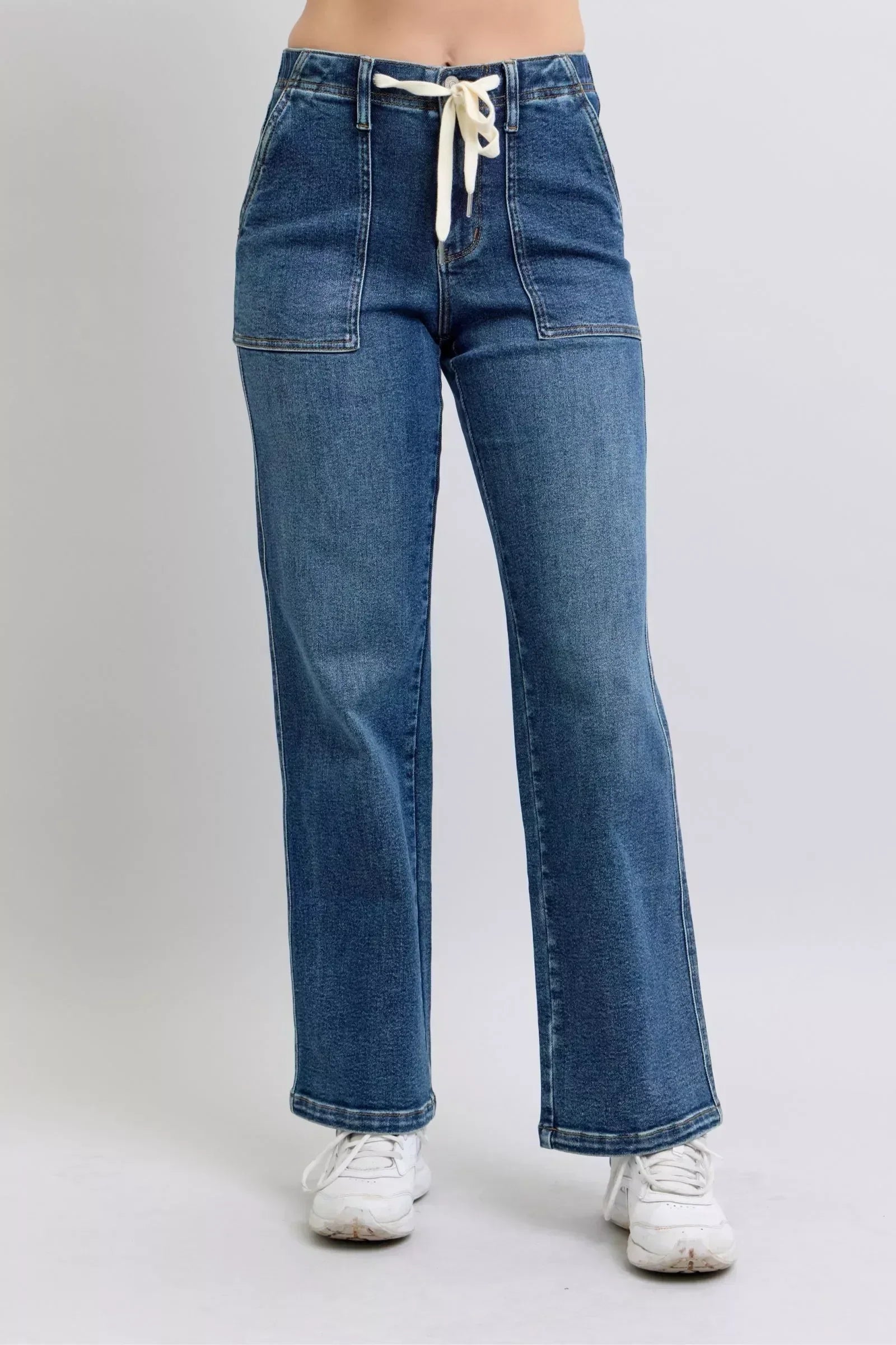 High-waisted blue denim jeans with front pockets and drawstring tie, worn with white sneakers